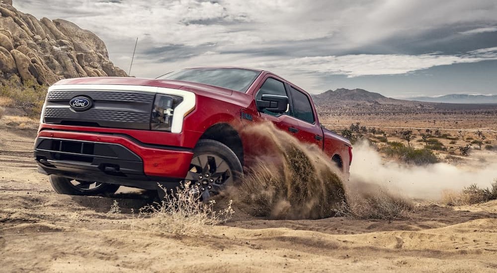 A red 2024 Ford F-150 Lightning is shown driving off-road.