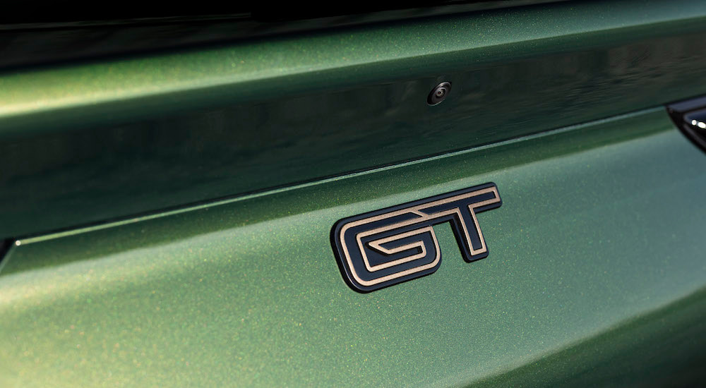 A close-up shows the badge on a green 2024 Ford Mustang Mach-E GT.