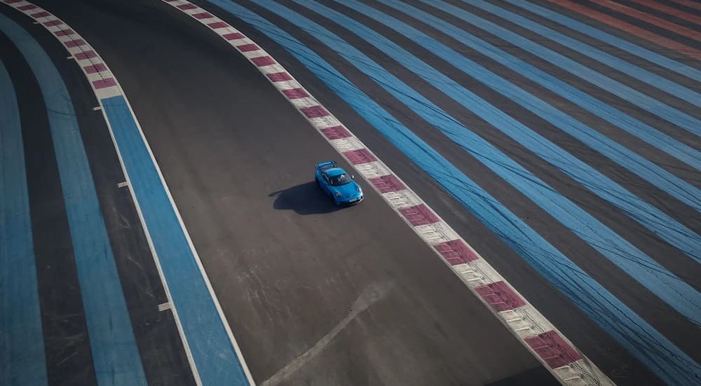 An aerial view of a blue 2024 Porsche 911 GT3 riding on a track is shown.