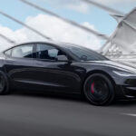 A black 2024 Tesla Model 3 Performance driving over a bridge.