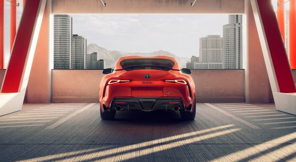 An orange 2024 Toyota GR Supra is shown parked in a parking garage near city buildings.
