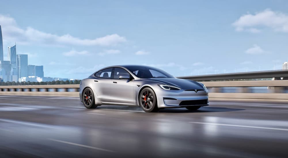 A silver 2025 Tesla Model S Plaid is shown driving on a bridge.