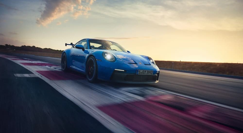 A blue 2024 Porsche 911 GT3 is shown driving on a racetrack.