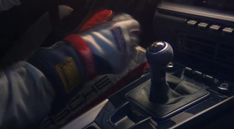 A driver is shown reaching for the gear shifter knob.