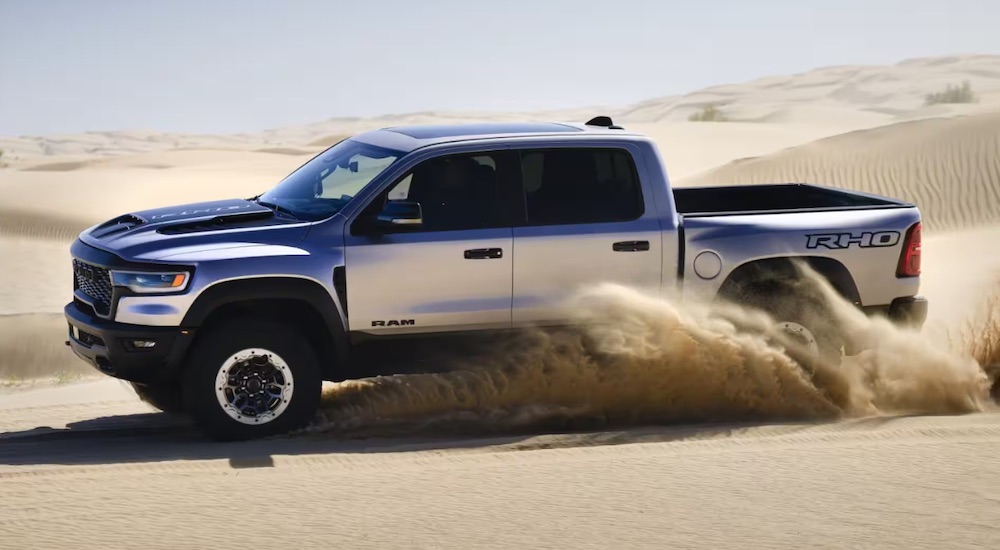 A white and black 2025 Ram 1500 RHO driving in a desert from a dealer with Ram trucks for sale.