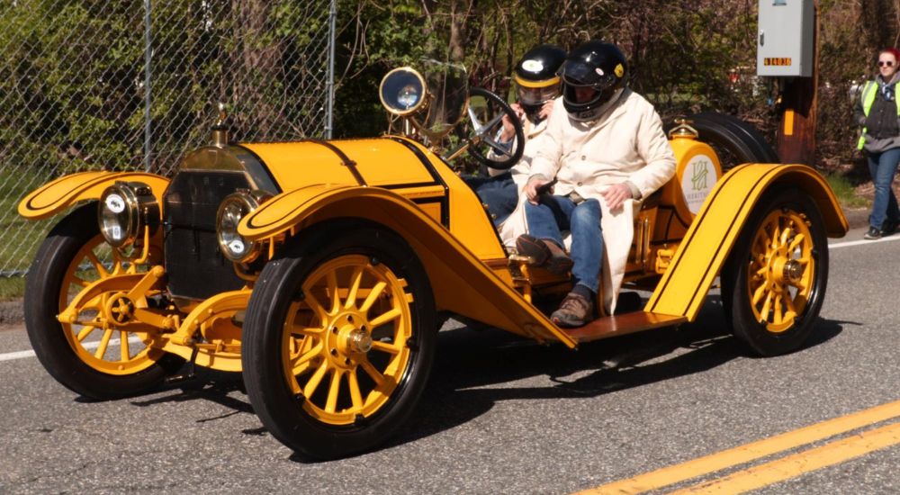 A yellow 1912 Mercer 35 Raceabout is shown parked on pavement.