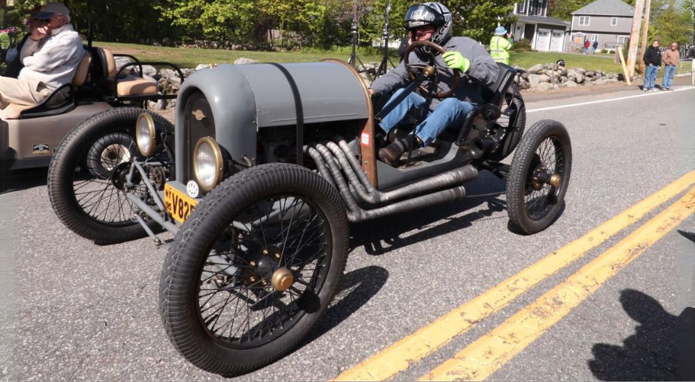A person is shown driving a grey 1915 Ford Model T Speedster.