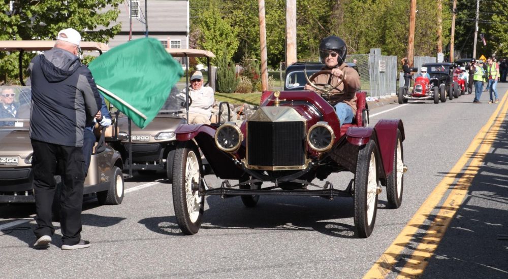 A maroon 1923 Ford Model T Runabout is shown next to a green flag.