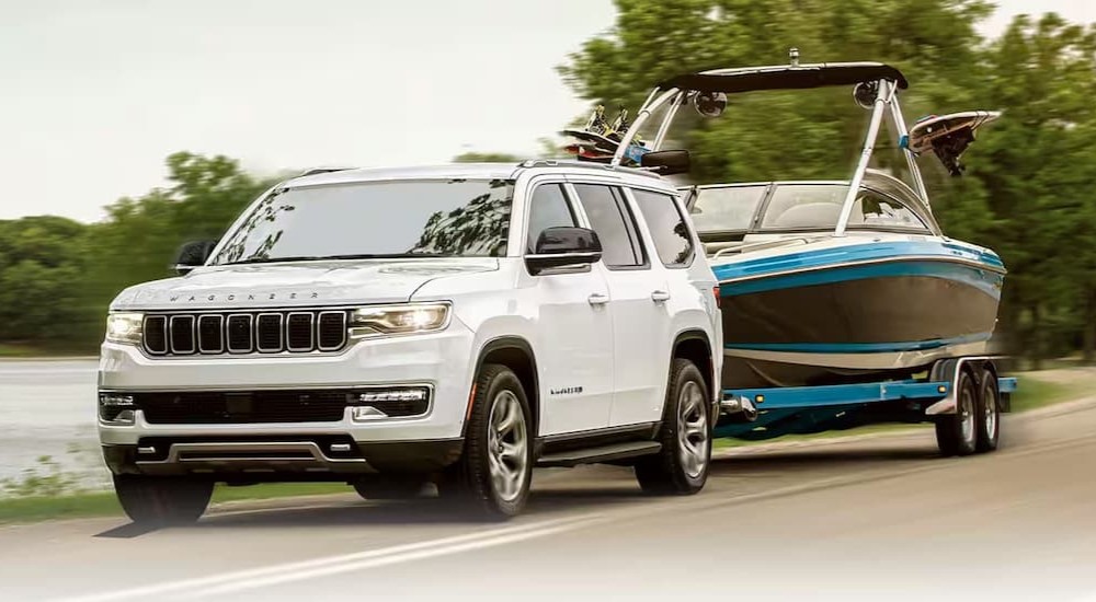 A white 2024 Jeep Wagoneer for sale is shown towing a boat.