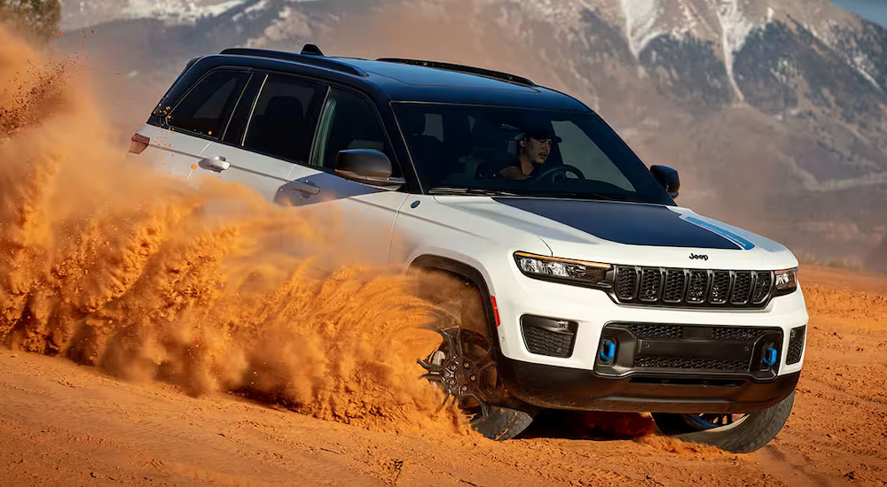 A white 2024 Jeep Grand Cherokee Trailhawk 4xe kicking up sand while off-roading down a hill.