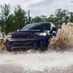 A blue 2024 Jeep Grand Cherokee Trailhawk 4xe splashing through water while off-roading.