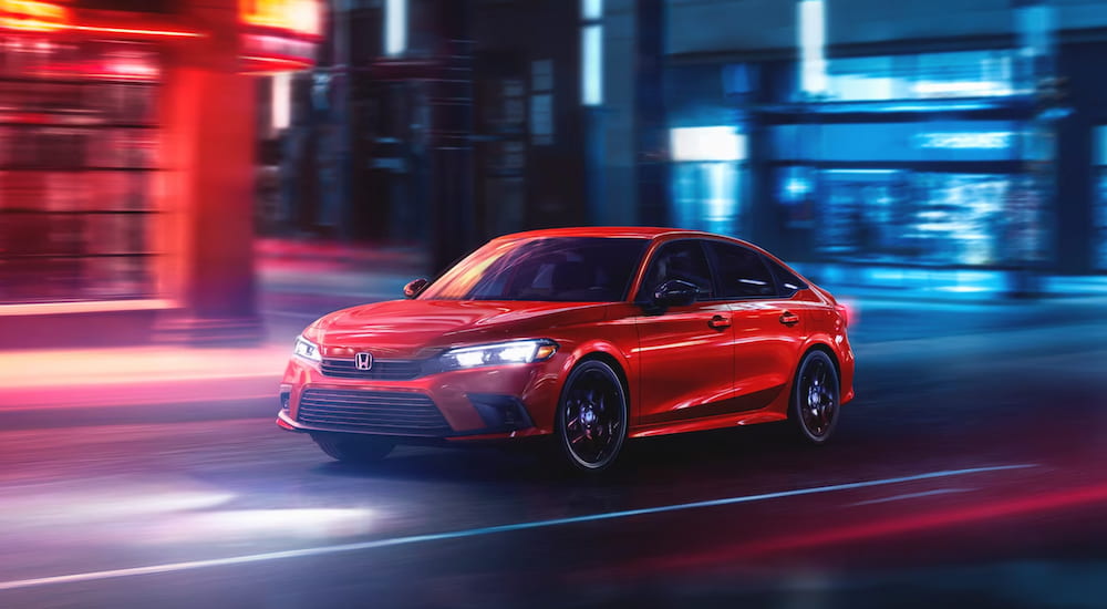 A red 2024 Honda Civic driving in a city from a dealer with a Honda Civic Hatchback for sale.