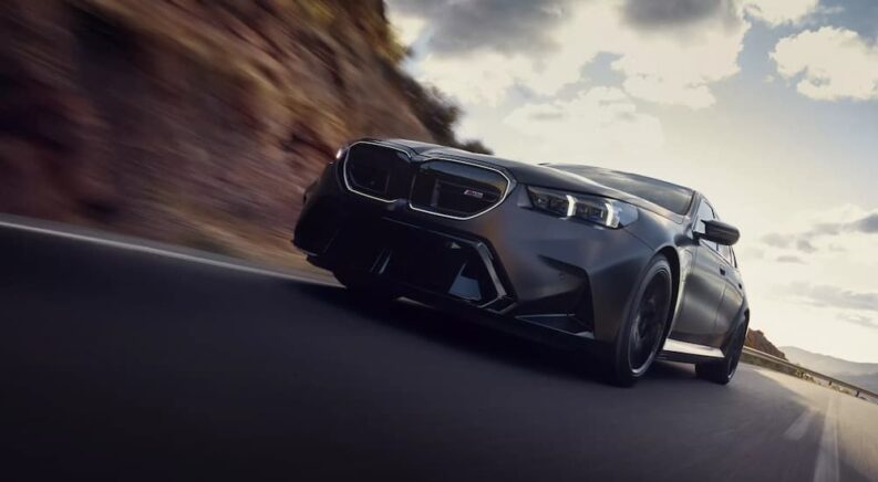 A gray 2025 BMW M5 is shown driving on a highway.