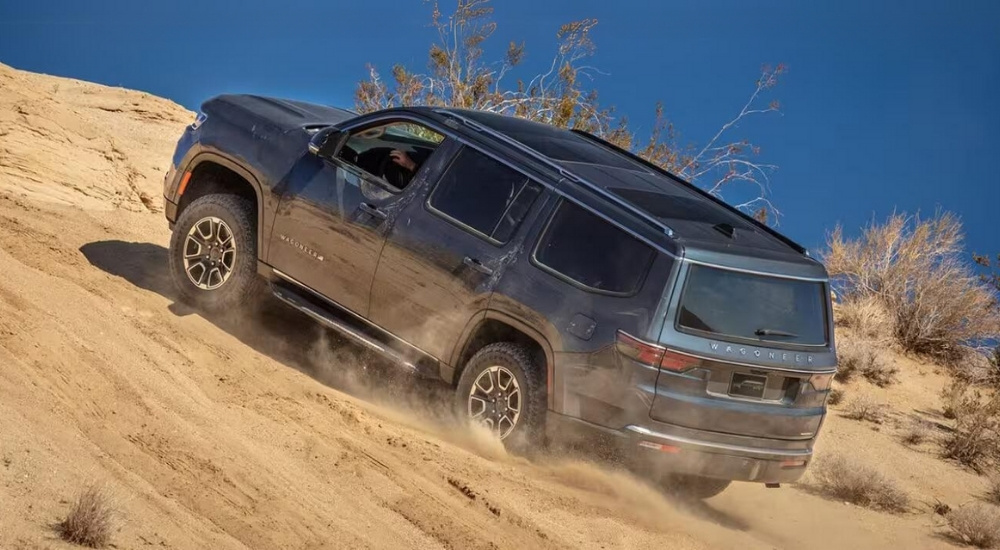 A grey 2024 Jeep Wagoneer is shown driving up a sand dune.