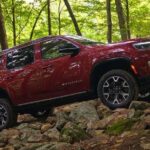 A red 2023 Jeep Wagoneer for sale is shown off-roading in a forest.