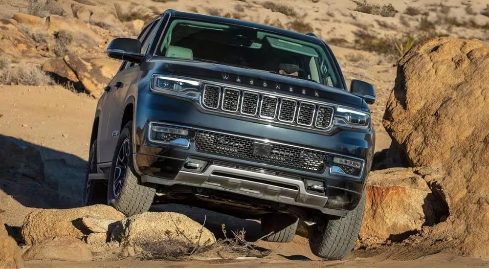 A grey 2024 Jeep Wagoneer is shown crawling over rocks.