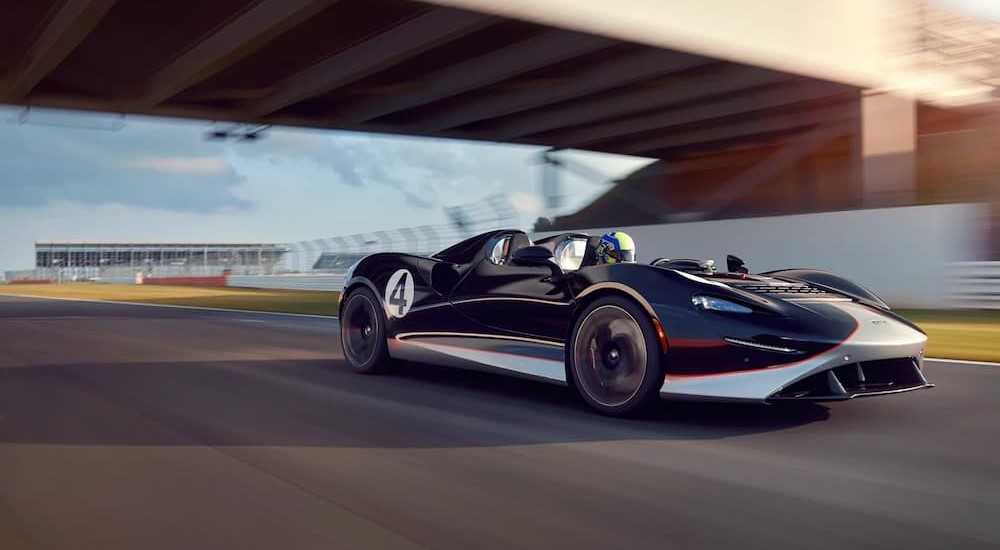 A black and white McLaren Elva is shown driving on a racetrack.