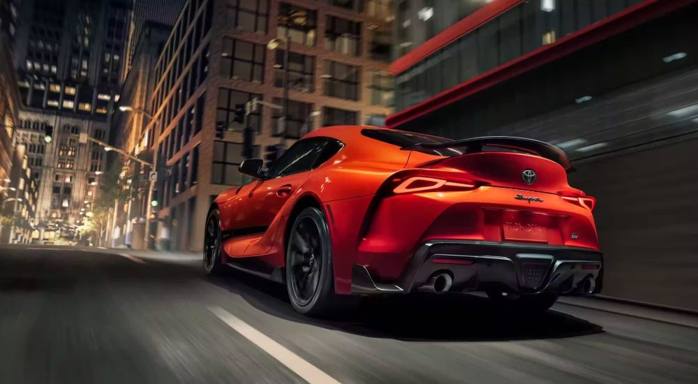 Rear view of an orange 2024 Toyota GR Supra 45th Anniversary Edition driving in a city. 