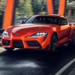 An orange 2024 Toyota GR Supra driving from a Toyota dealer.