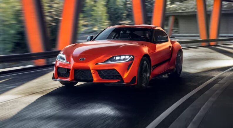 An orange 2024 Toyota GR Supra driving from a Toyota dealer.