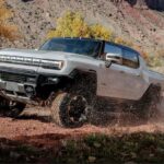 A white 2024 GMC Hummer EV Pickup is shown driving off-road.