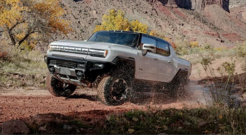 A white 2024 GMC Hummer EV Pickup is shown driving off-road.