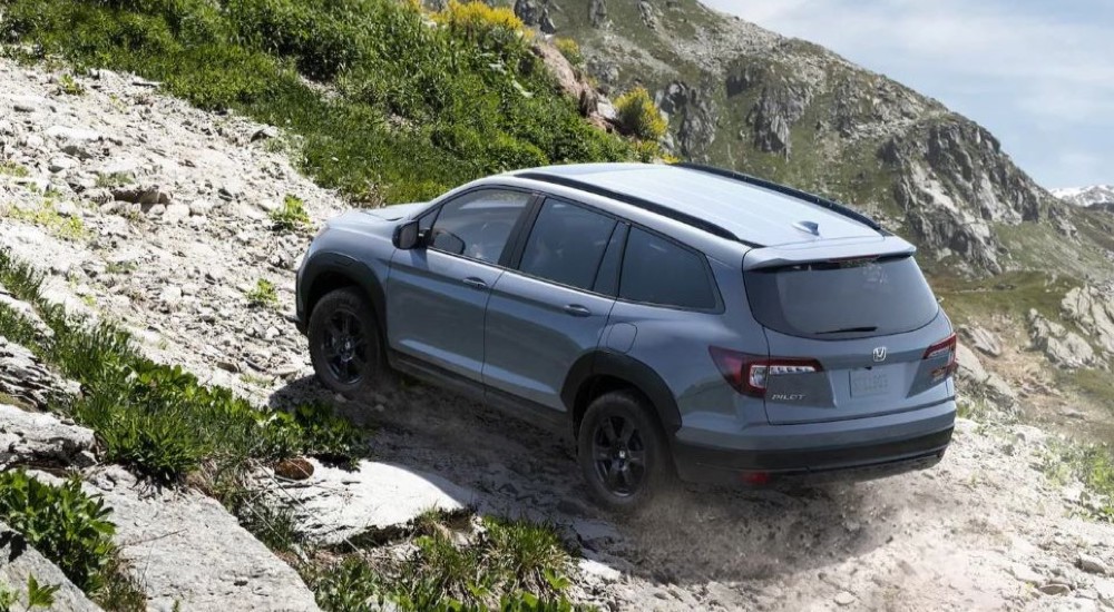 A grey 2022 Honda Pilot TrailSport driving up a rocky hillside.