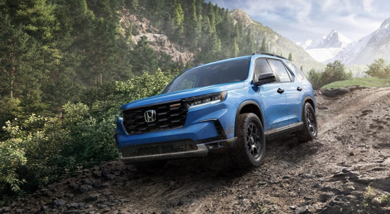 A blue 2025 Honda Pilot TrailSport off-roading down a rocky trail.