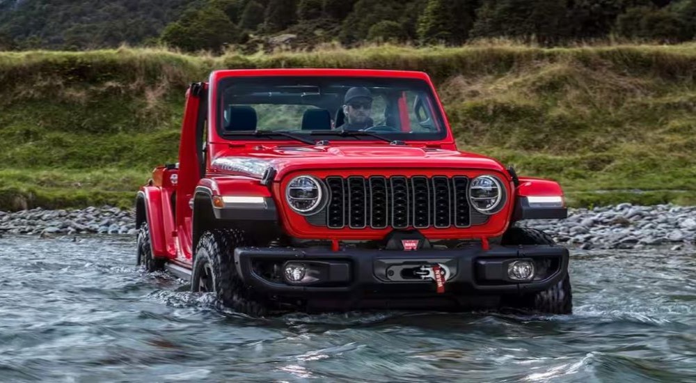 A red 2024 Jeep Wrangler Rubicon Unlimited fording a shallow river.