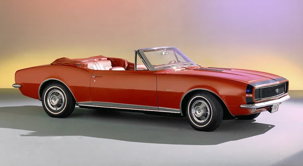 A red 1967 Chevy Camaro convertible is shown parked on a showroom floor.