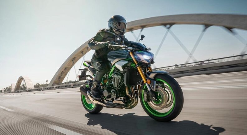 A green 2024 Kawasaki Z900 is shown riding on a bridge after visiting a motorcycle dealer.