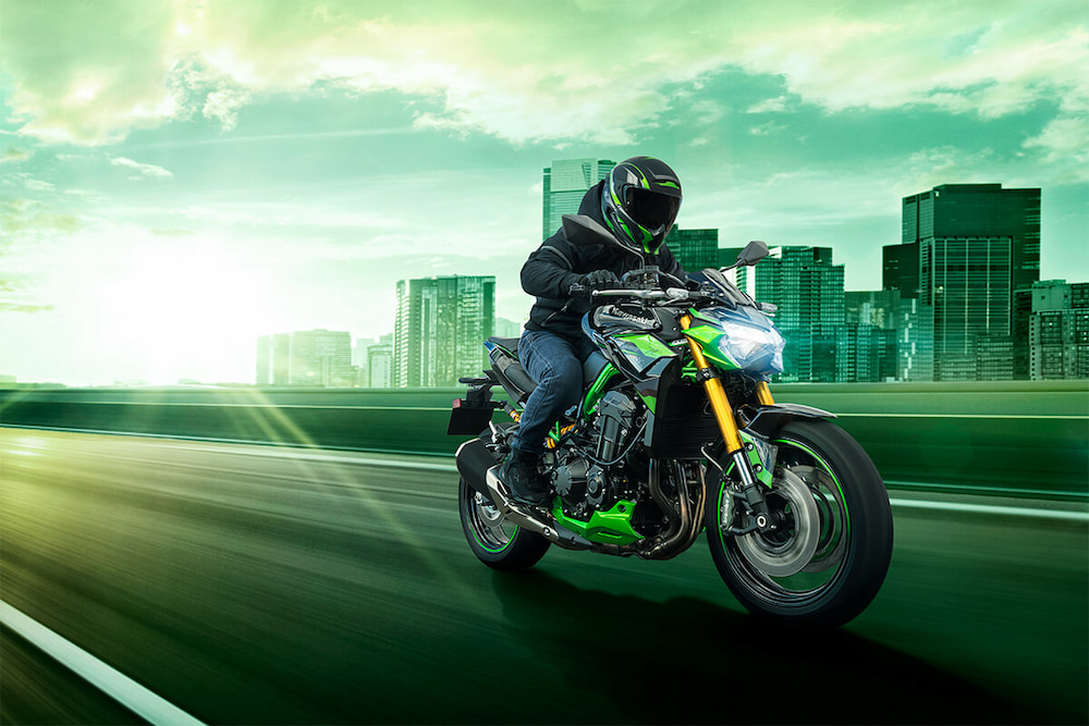 A green 2024 Kawasaki Z900 SE is shown driving near a city.