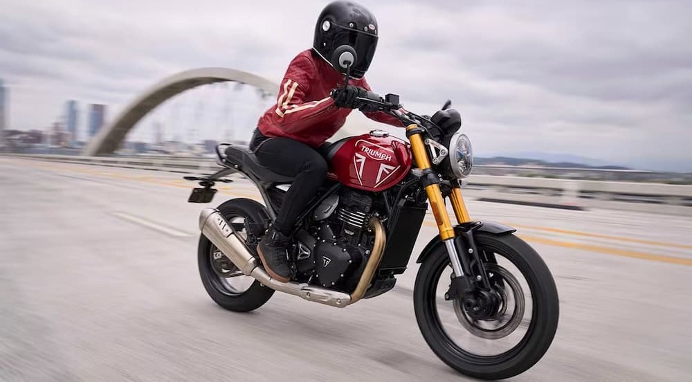 A red 2024 Triumph Speed 400 is shown driving on a bridge.