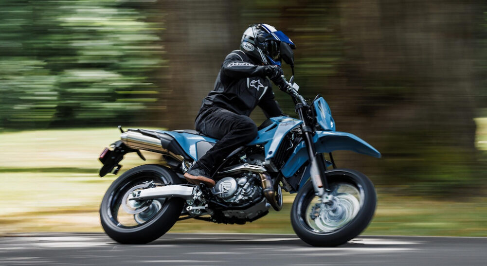 A blue 2025 Suzuki DR-Z4SM is shown riding around a corner.