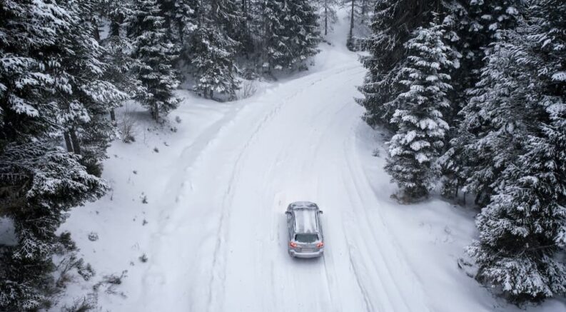 An aerial view of an SUV driving on a snowy road.