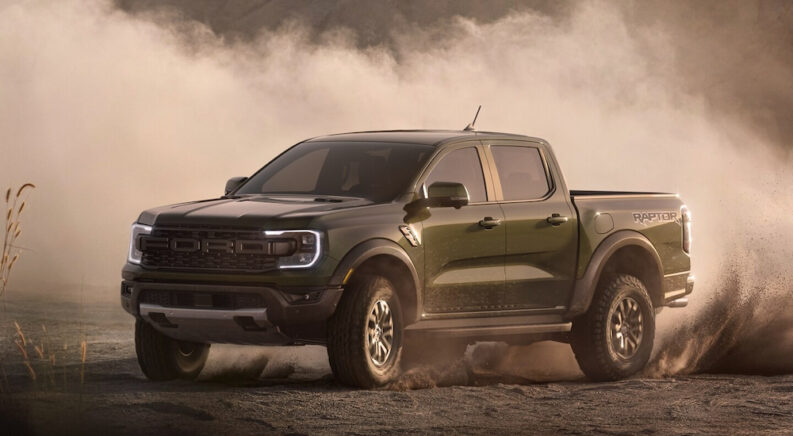 An army green 2024 Ford Ranger Raptor kicking up sand while off-roading.