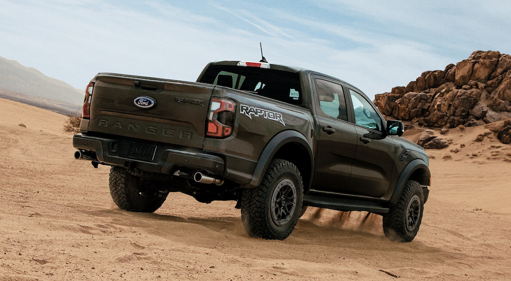 Rear view of an army green 2024 Ford Ranger Raptor driving over sand dunes.