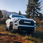 Low angle view of a white 2025 Toyota Sequoia TRD Pro parked off-road by a camp.