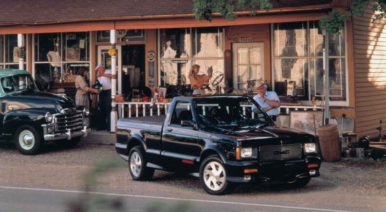 A black 1991 GMC Syclone parked in front of a small-town storefront.