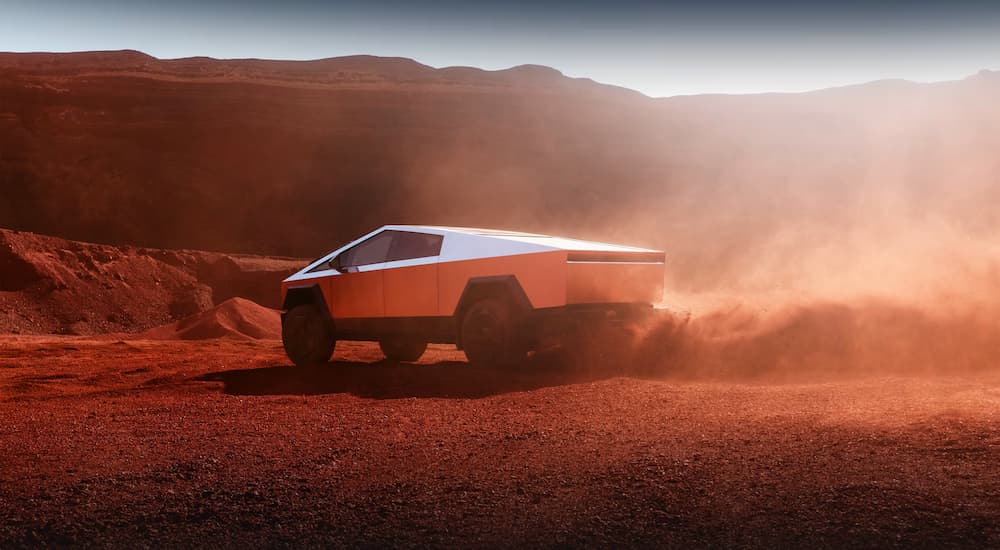 Rear view of a 2024 Tesla Cybertruck kicking up dust driving through a red landscape.