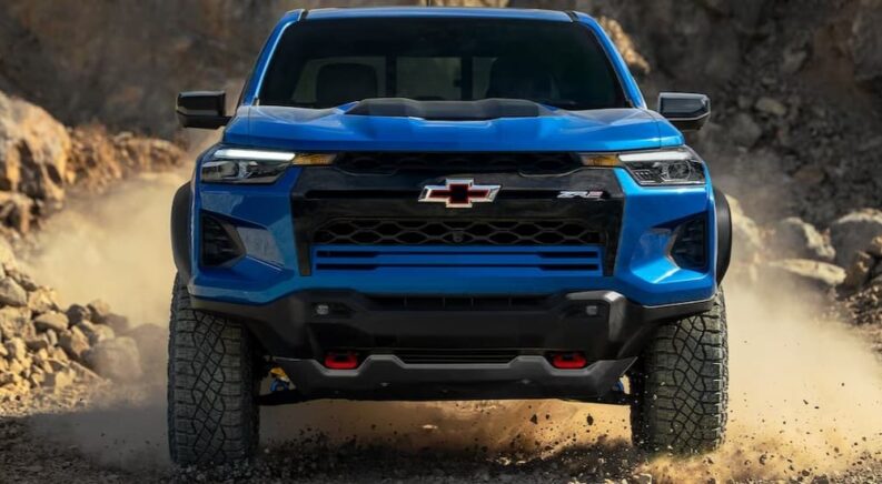 A blue 2024 Chevy Silverado 1500 ZR2 is shown driving off-road after visiting a Chevy dealer.