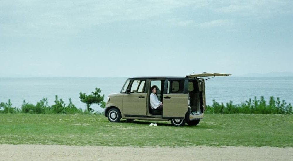 A tan 2024 Honda N-Box is shown parked near an ocean.