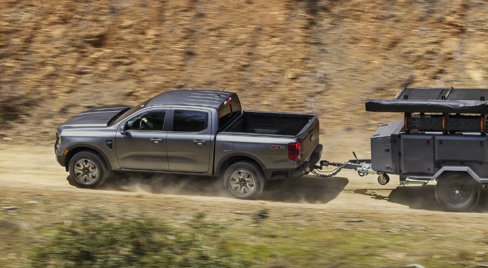 A grey 2025 Ford Ranger Raptor towing a small trailer on a dirt trail.