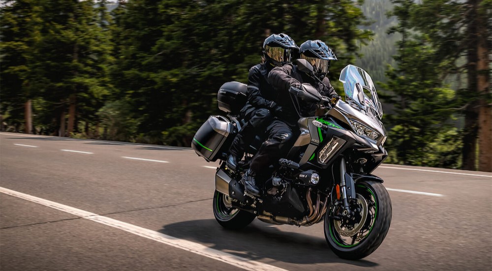 Two people are shown riding on a green and black 2025 Kawasaki Versys 1100.