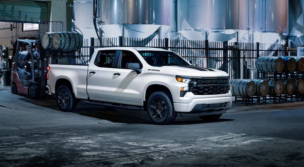 A white Chevy Silverado 1500 Rally Edition is shown parked near wooden barrels.