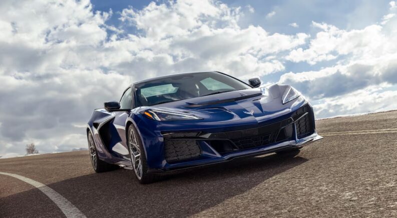 A blue 2025 Chevy Corvette ZR1 is shown driving on a cloudy day.