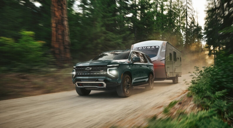 A green 2025 Chevy Tahoe Z71 is shown from the front while towing a trailer.