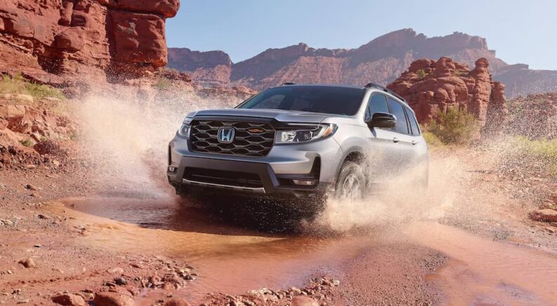 A grey 2025 Honda Passport TrailSport driving off-road through a shallow puddle.