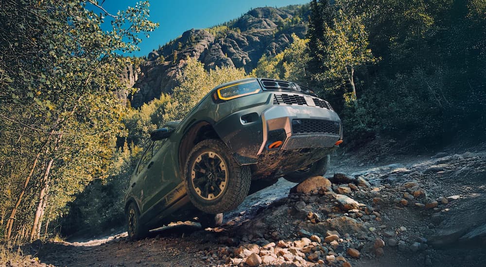 A green 2026 Honda Passport TrailSport driving off-road up a hill.