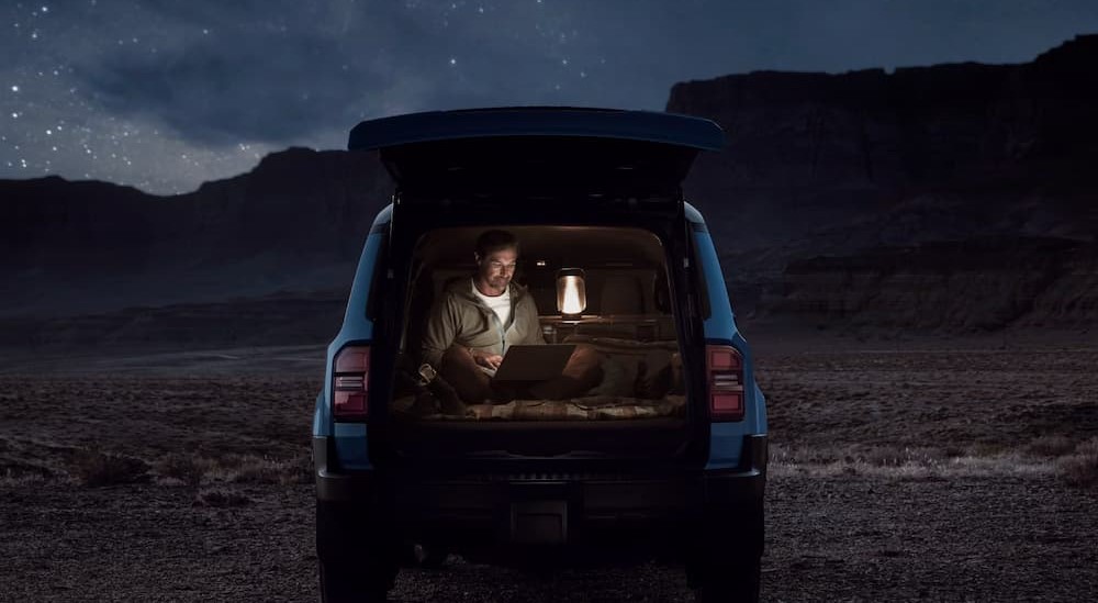 A person is shown sitting in the rear cargo area of  blue 2025 Toyota Land Cruiser.